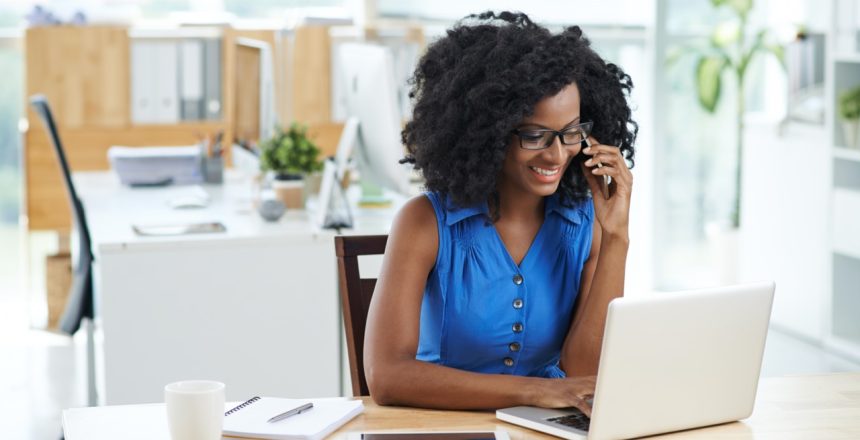 Cheerful business lady talking on the phone when using laptop